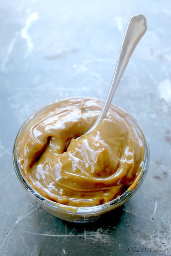 caramel sauce in a clear glass bowl with a spoon in it on a rustic metal surface