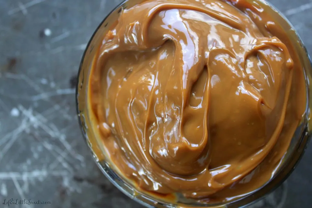 overhead view of caramel sauce in a clear glass bowl on a rustic metal surface