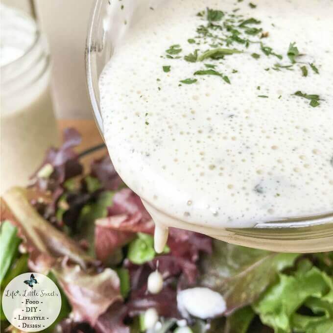 buttermilk ranch dressing being poured out of a mason jar over a green salad