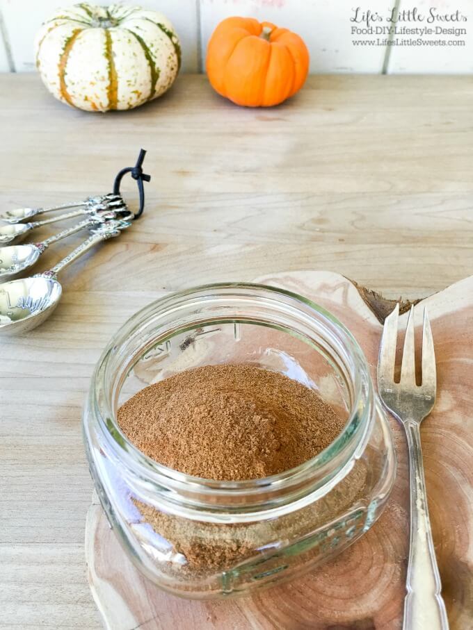 Pumpkin Spice Mix in a jar on a wood table with small pumpkins in the background