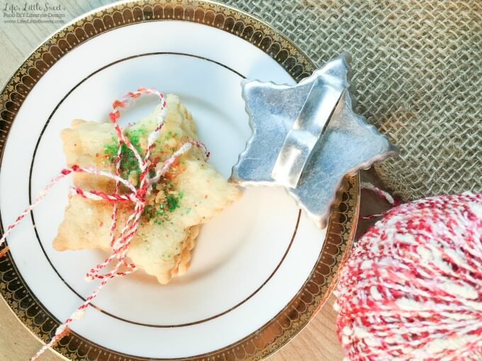 sand tart cookies tied up with red and white twine on a gold rimmed plate with a star shaped antique cookie cutter