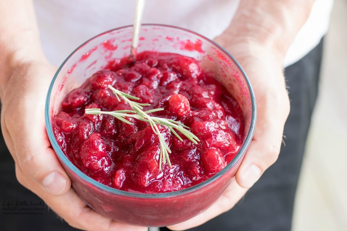 a clear bowl of Rosemary-Infused Cranberry Sauce being held by hands with rosemary on top