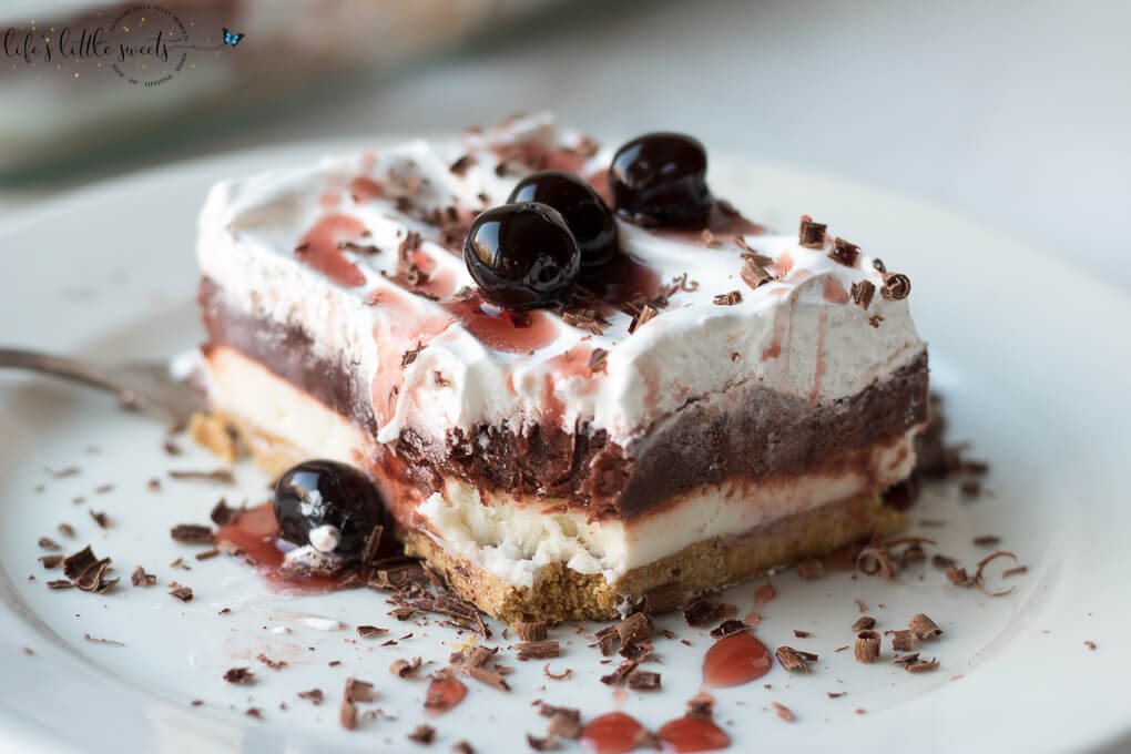 This Red Velvet Lasagna Dessert Recipe is a layered, no bake desert recipe with a crunchy graham cracker crust, cream cheese layer, red chocolate pudding layer and topped with Cool Whip, chocolate shavings and cherry syrup. This dessert has 4 delicious, velvety layers and uses a 9 x 13 inch pan, making the perfect dessert to bring to a gathering. #cherries #lush #lasagna #chocolatepudding #chocolate #coolwhip #grahamcracker #nobake #creamcheese