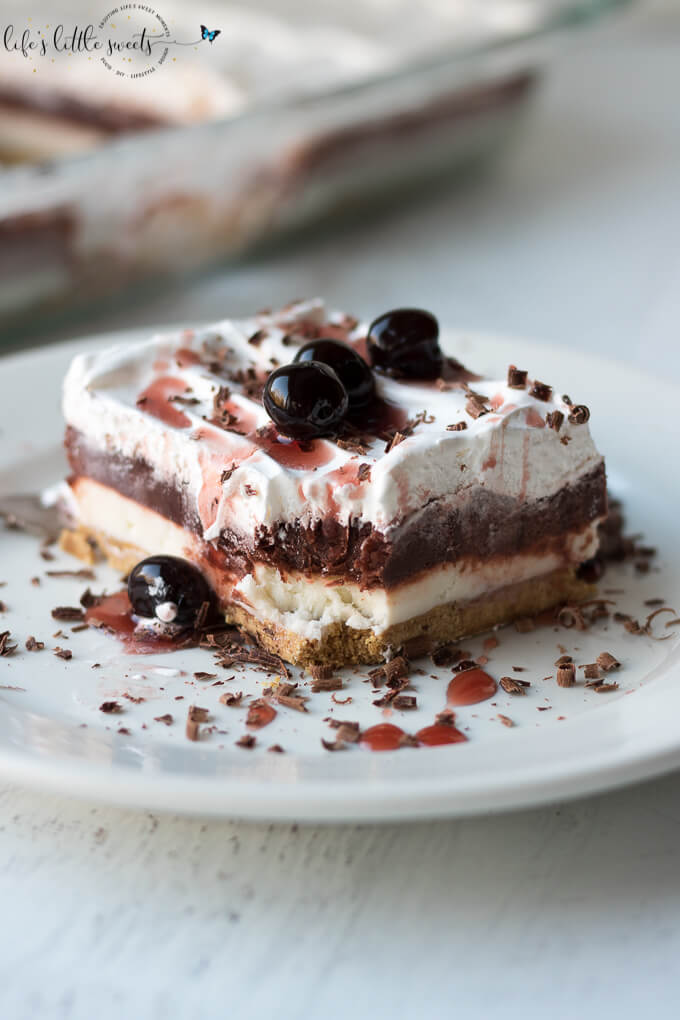 This Red Velvet Lasagna Dessert Recipe is a layered, no bake desert recipe with a crunchy graham cracker crust, cream cheese layer, red chocolate pudding layer and topped with Cool Whip, chocolate shavings and cherry syrup. This dessert has 4 delicious, velvety layers and uses a 9 x 13 inch pan, making the perfect dessert to bring to a gathering. #cherries #lush #lasagna #chocolatepudding #chocolate #coolwhip #grahamcracker #nobake #creamcheese