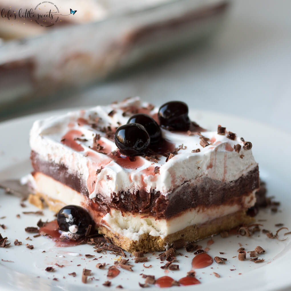 This Red Velvet Lasagna Dessert Recipe is a layered, no bake desert recipe with a crunchy graham cracker crust, cream cheese layer, red chocolate pudding layer and topped with Cool Whip, chocolate shavings and cherry syrup. This dessert has 4 delicious, velvety layers and uses a 9 x 13 inch pan, making the perfect dessert to bring to a gathering. #cherries #lush #lasagna #chocolatepudding #chocolate #coolwhip #grahamcracker #nobake #creamcheese