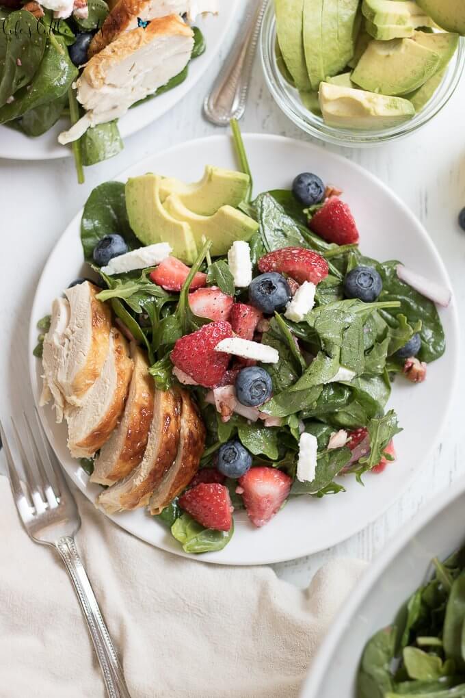 This Strawberry Salad Recipe has fresh strawberries, baby spinach, arugula, chopped pecans, feta with a light lemon vinaigrette dressing. It is garnished with blueberries, sliced ripe avocado and optional chicken. Enjoy it in the Summer months or year round! #recipe #strawberries #chicken #blueberries #avocado #feta #pecans #arugula #lemon #salad 