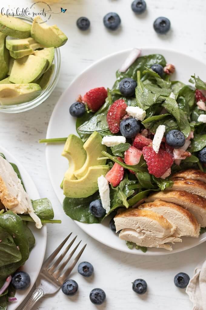This Strawberry Salad Recipe has fresh strawberries, baby spinach, arugula, chopped pecans, feta with a light lemon vinaigrette dressing. It is garnished with blueberries, sliced ripe avocado and optional chicken. Enjoy it in the Summer months or year round! #recipe #strawberries #chicken #blueberries #avocado #feta #pecans #arugula #lemon #salad 