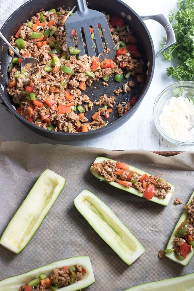 These Stuffed Zucchini Boats are a savory, delicious and complete dinner allowing you to get your dose of vegetables. Filled with your favorite meat, in this case, lean ground turkey, they also have bell peppers, onions and grated cheese. This low-carb dinner is a great way to use up all that garden zucchini! #zucchini #zucchiniboats #squash #turkey #cheese #parsley #onions #peppers