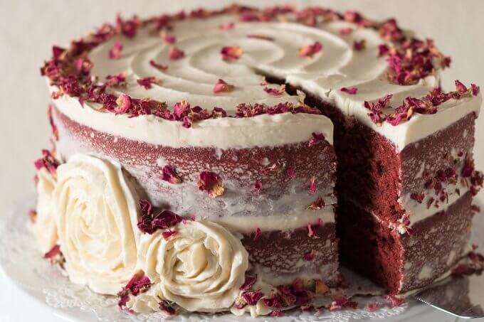 This Red Velvet Cake Recipe is a tall, dramatic, 2-tiered cake recipe that uses red cocoa, espresso powder, and is topped with a delicious cream cheese frosting. This cake is festive, attractive and perfect for year-round celebrations, birthdays and gatherings! #redvelvet #cake #recipe #creamcheese #frosting #roses #rosecake #nakedcake