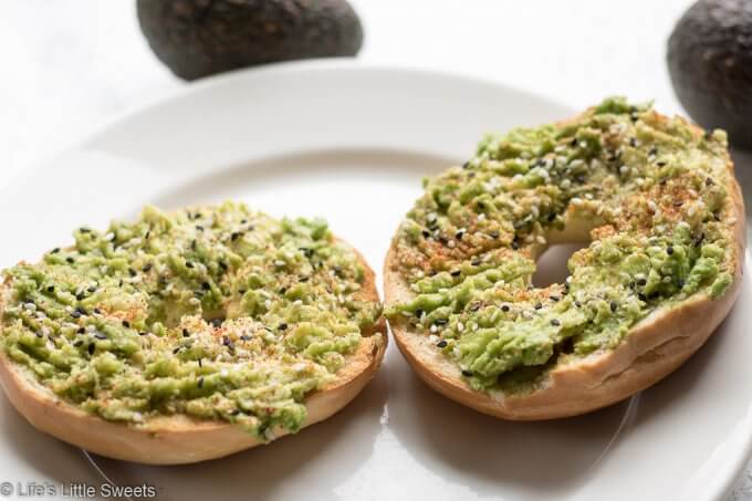 This Avocado Bagel Toast makes the perfect, satisfying and savory breakfast to start the day or mid-day snack. It has mashed, ripe, fresh, avocado, tuxedo sesame seeds, kosher salt, fresh ground peppercorn medley and smoked paprika sprinkled on top. #avocadobageltoast #breakfasts #snacks #recipe #sesameseeds #tuxedosesameseeds #smokedpaprika #koshersalt #salt #savory