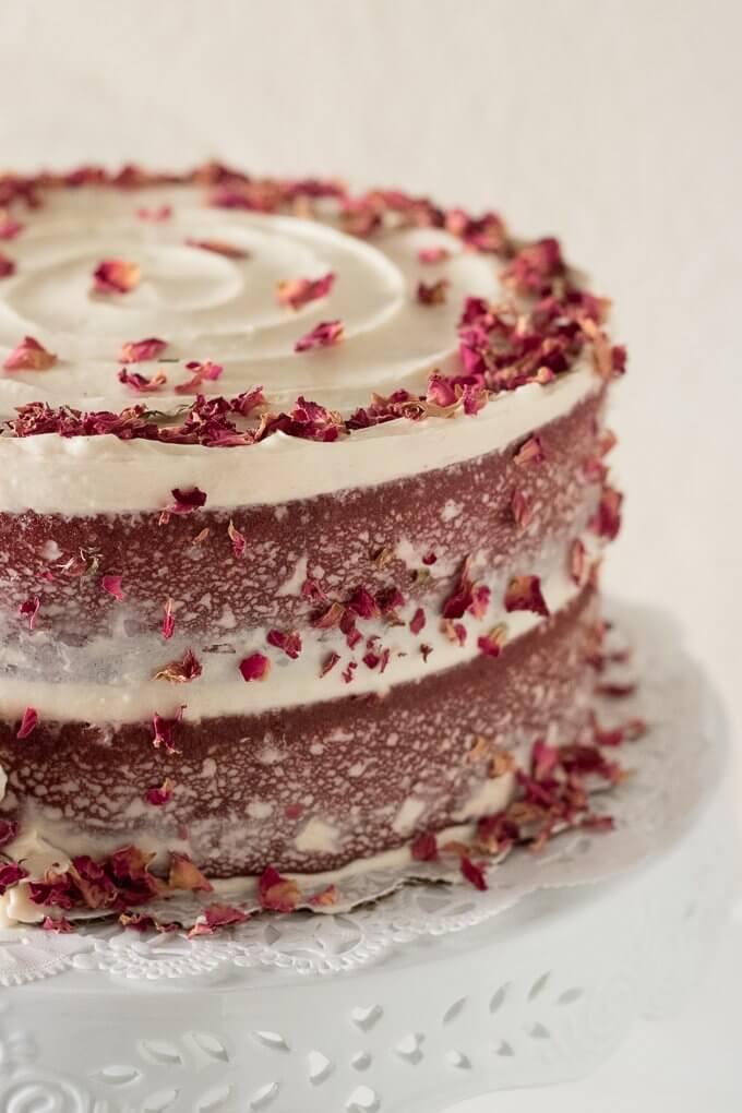 This Red Velvet Cake Recipe is a tall, dramatic, 2-tiered cake recipe that uses red cocoa, espresso powder, and is topped with a delicious cream cheese frosting. This cake is festive, attractive and perfect for year-round celebrations, birthdays and gatherings! #redvelvet #cake #recipe #creamcheese #frosting #roses #rosecake #nakedcake