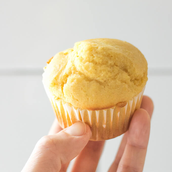 a fresh yellow Cornbread Muffin being held in front of white subway tile backsplash