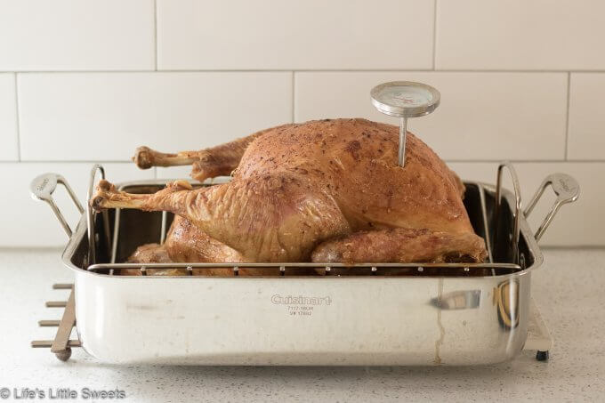 Turkey cooling on a trivet on the counter of a white kitchen in a stainless steel pan
