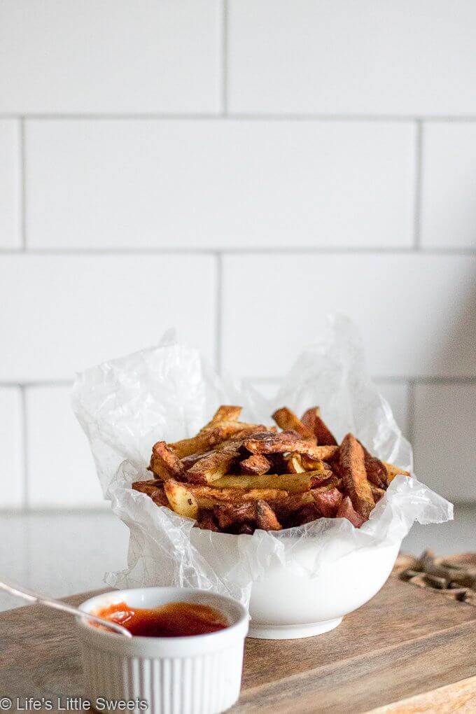 a small white ramekin ceramic dish with a white bowl of crisp fries made in an air fryer with a white subway tile in the background on a white kitchen countertop