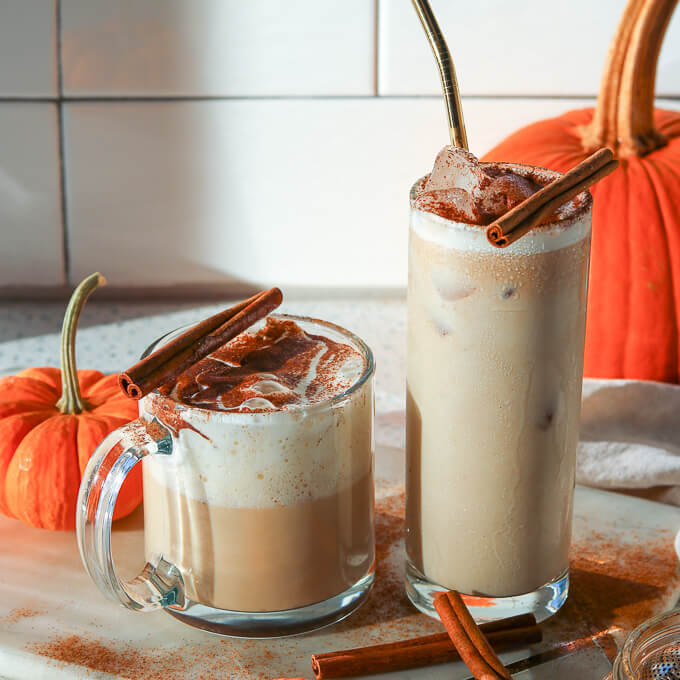 Pumpkin Spice Latte iced and hot in a white kitchen with orange pumpkins in the background