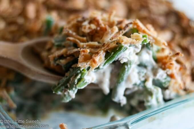 Green Bean Casserole being served out of a 9x13-inch clear baking dish with a wooden spoon