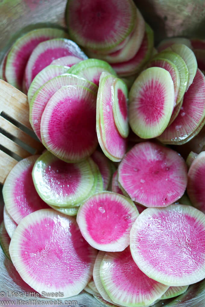 Watermelon Radish slices mixed with seasonings in a metal mixing bowl