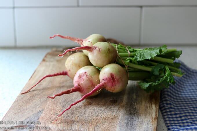 Watermelon Radish in a bunch on a board with a tea towel