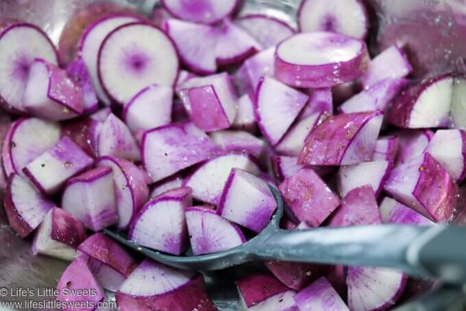 Purple Daikon Radishes cut up and mixed with spices and oil in a metal mixing bowl