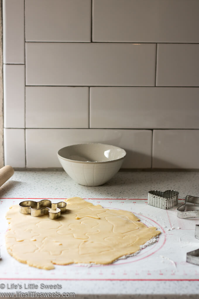 sugar cookie dough on a pastry mat with metal cookie cutters white subway tile