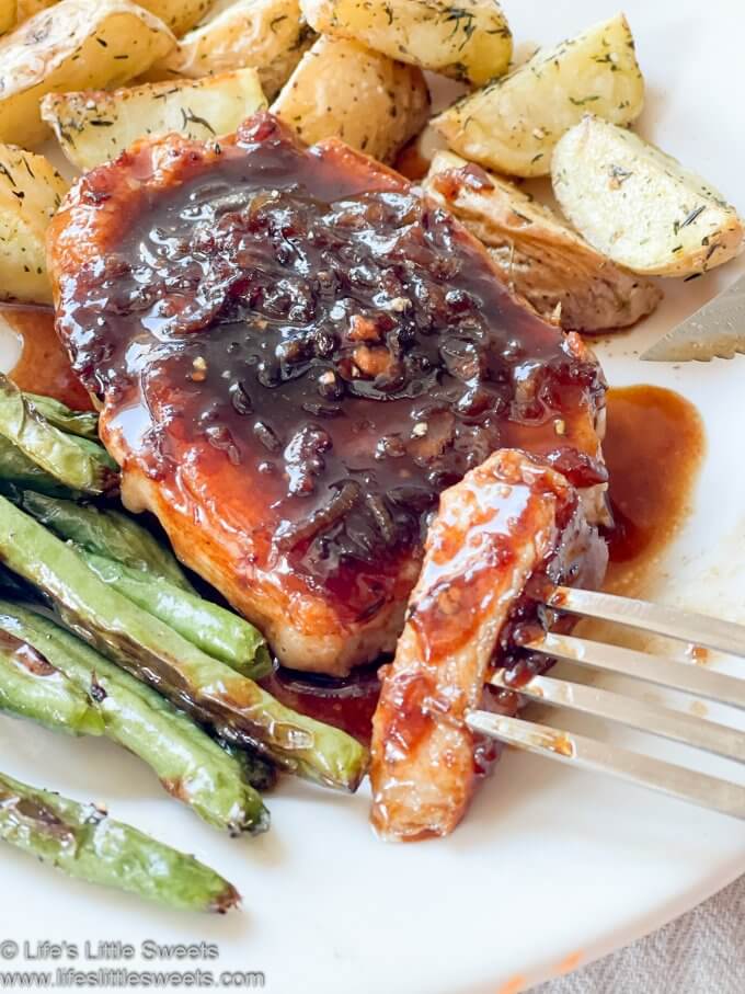 Bite of pork chop on a fork, green beans on a white plate with roasted potatoes