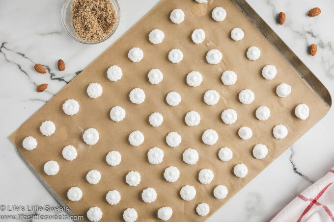 a parchment lined baking sheet with almond meringue kisses piped onto it