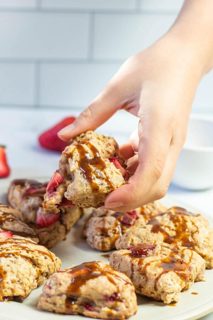 a hand picking up a strawberry scone off of a white plate in a white kitchen