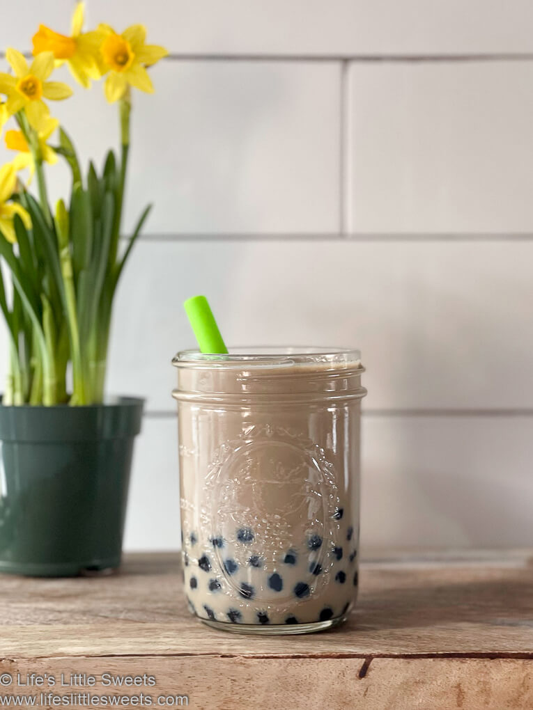bubble tea drink on a wood surface with a daffodil on the left side and subway tile in the background