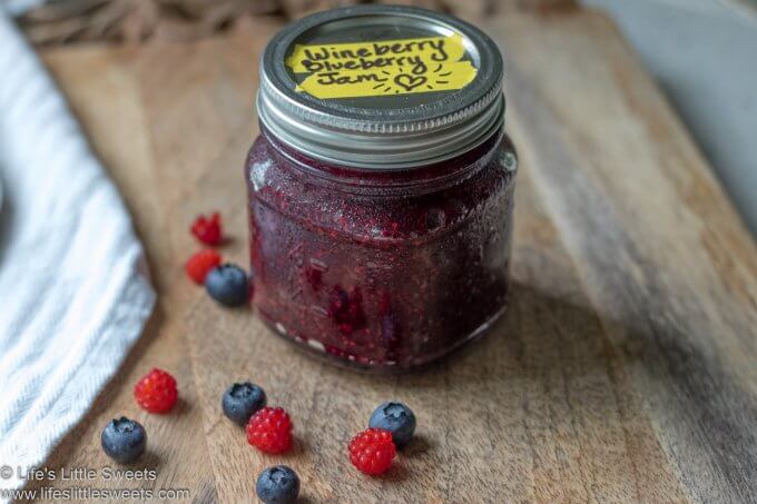 Red jam in a mason jar on a wood cutting board with a white tea towel