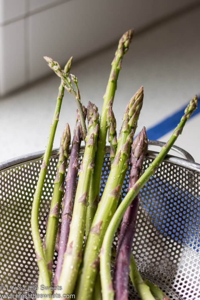 green and purple asparagus in a metal sieve in a white kitchen