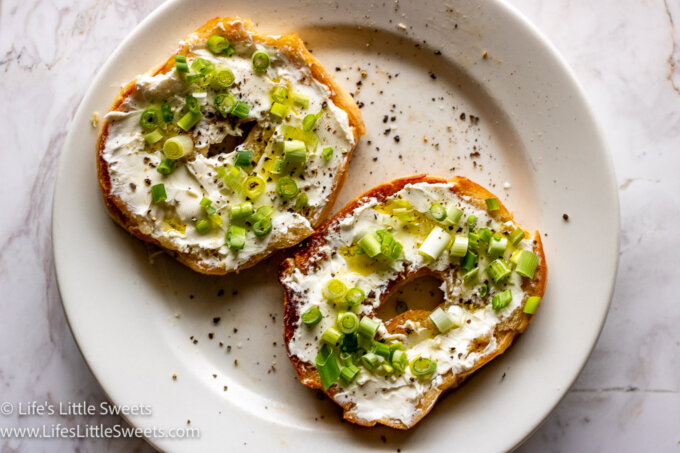 Bagel with Cream Cheese and Scallions on a white plate on a margle counter top