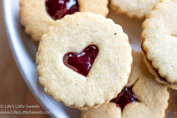 a photo of Linzer Cookies on a white plate with red jam overhead view