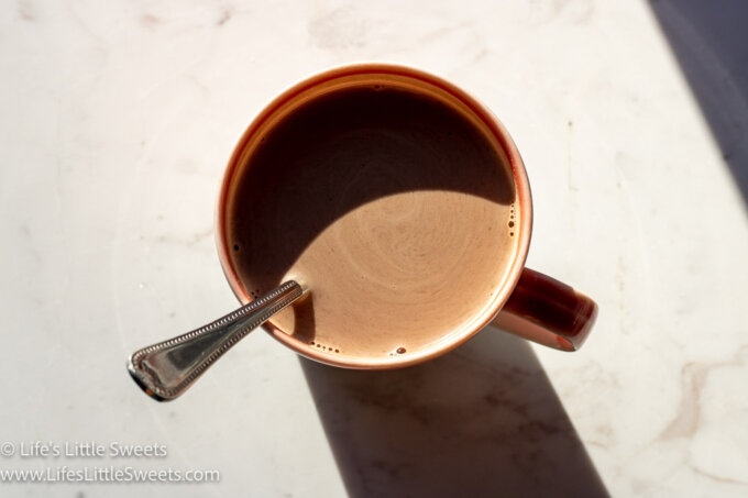 a mug with hot chocolate and a spoon on a marble surface