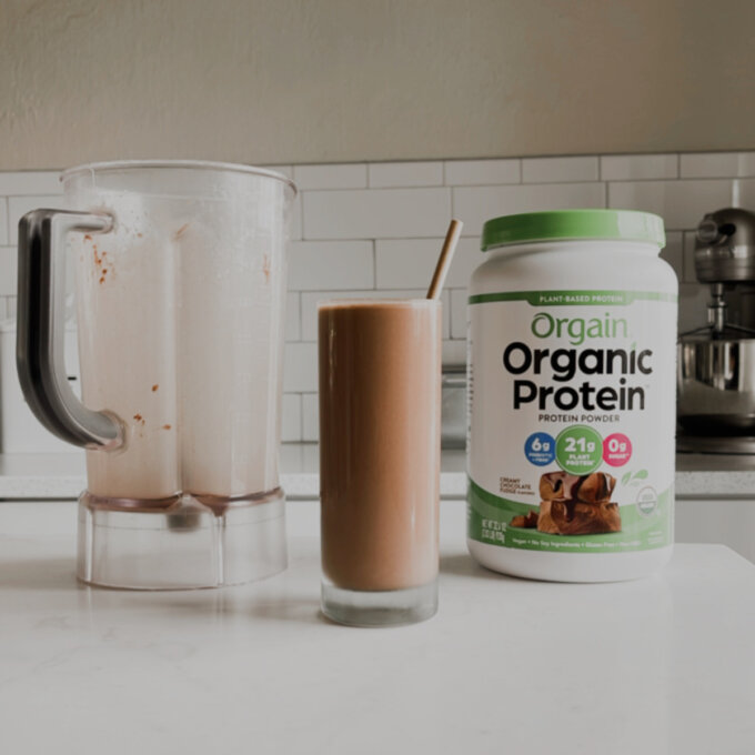 Square photo of Chocolate Protein Drink Recipe in a white kitchen with protein powder and a blender