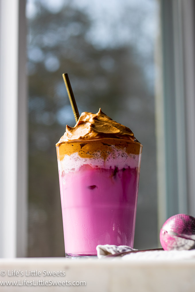 Dragon Fruit Whipped Coffee on a white marble countertop and a gold straw, layered pink and coffee drink