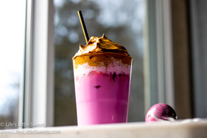 Dragon Fruit Whipped Coffee on a white marble countertop and a gold straw with a window behind