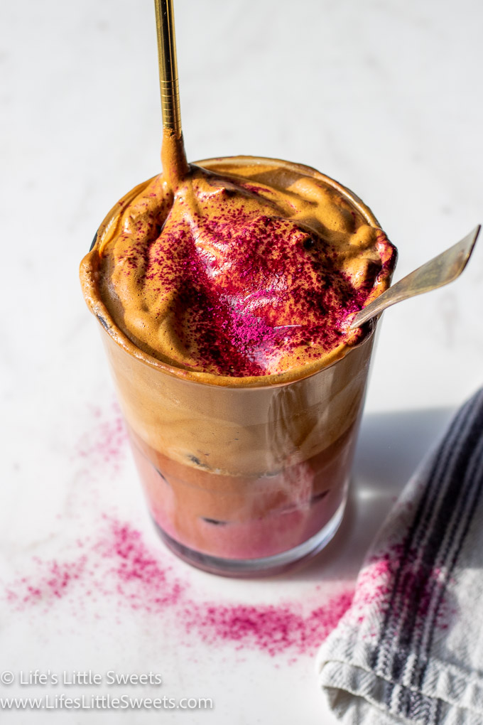 Whipped Coffee with pink milk on a white marble countertop and a gold straw with a dusting of pink powder