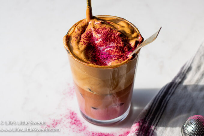 Whipped Coffee with pink milk on a white marble countertop and a gold straw with hot pink powder