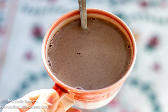 hand holding a pink and white mug with hot chocolate in it with a spoon