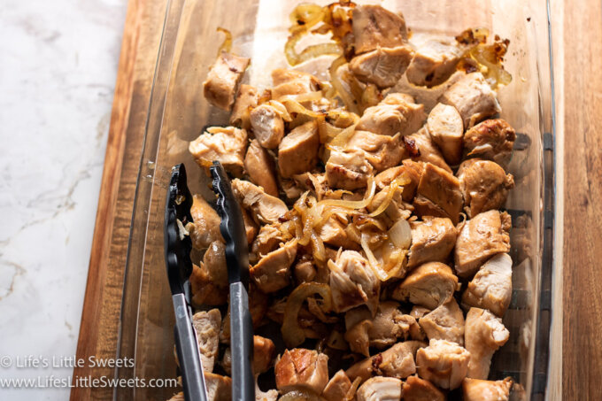 Stovetop Chicken and Onions in a clear platter with black tongs over a wood surface