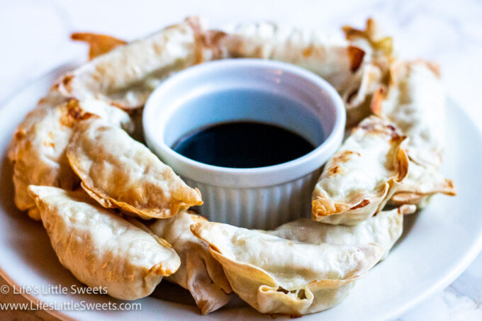 a white plate of air fried potstickers with soy sauce on a marble surface