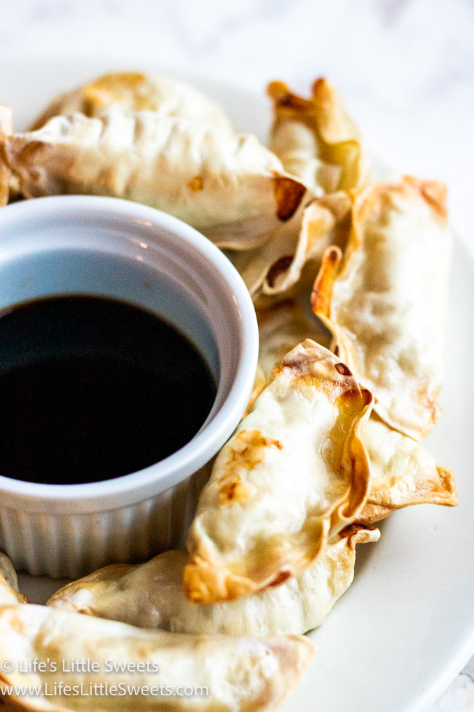 a white plate of air fried potstickers with soy sauce on a marble surface