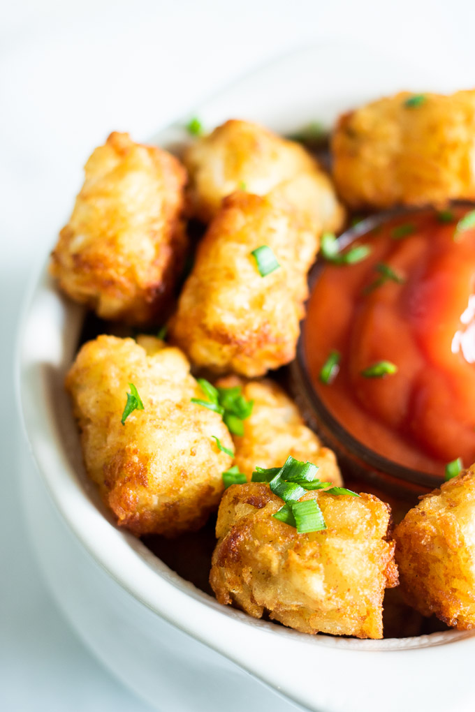 potato tots in a white bowl with ketchup and green chives on top