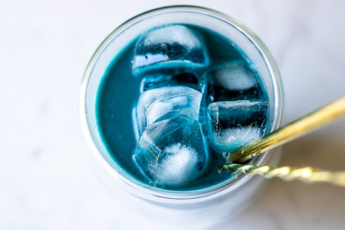 Butterfly Pea Flower Milk Tea overhead with ice on a white marble countertop with a gold straw