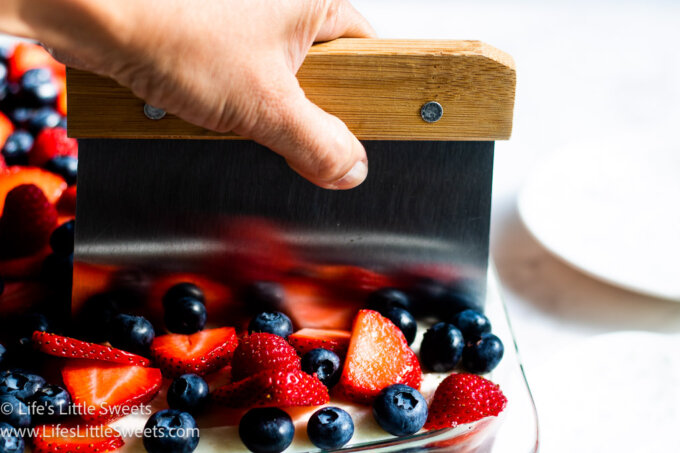 a 9x13-inch pan of cake with berries being sliced
