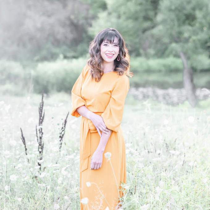 brunette woman in orange dress in a green field