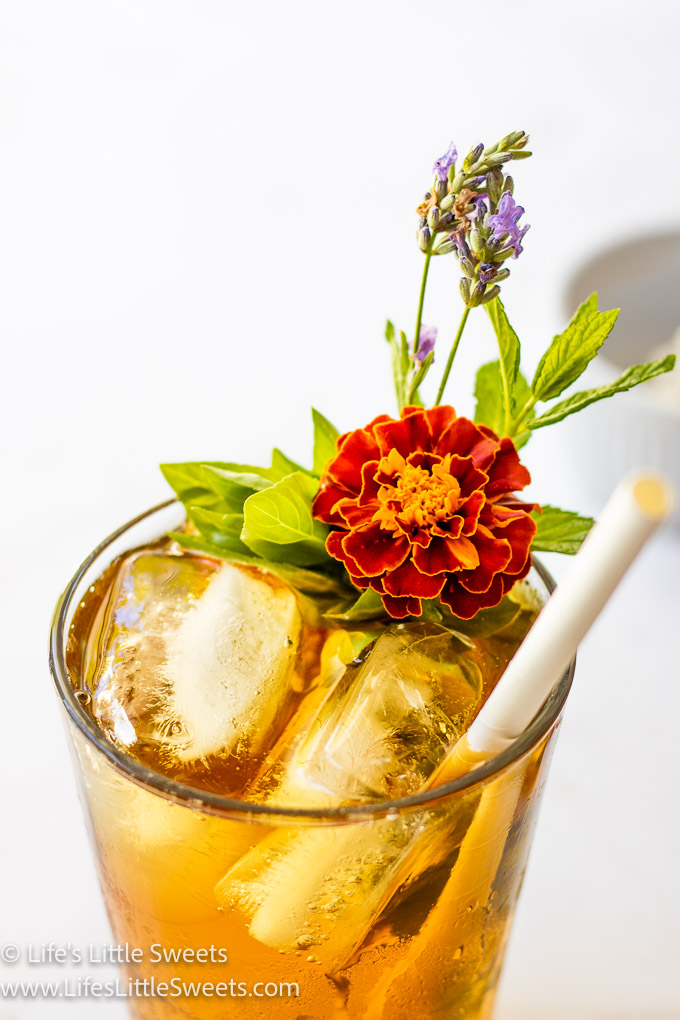 herbs and flowers in iced tea with a white paper straw