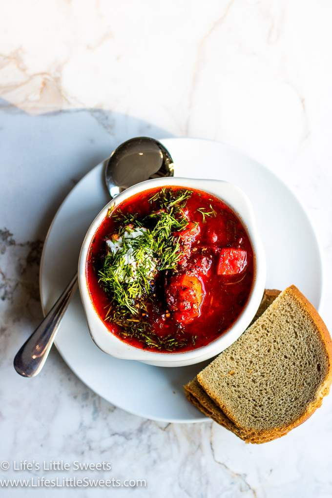 a bowl of red Borscht soup with dill and sour cream with rye bread