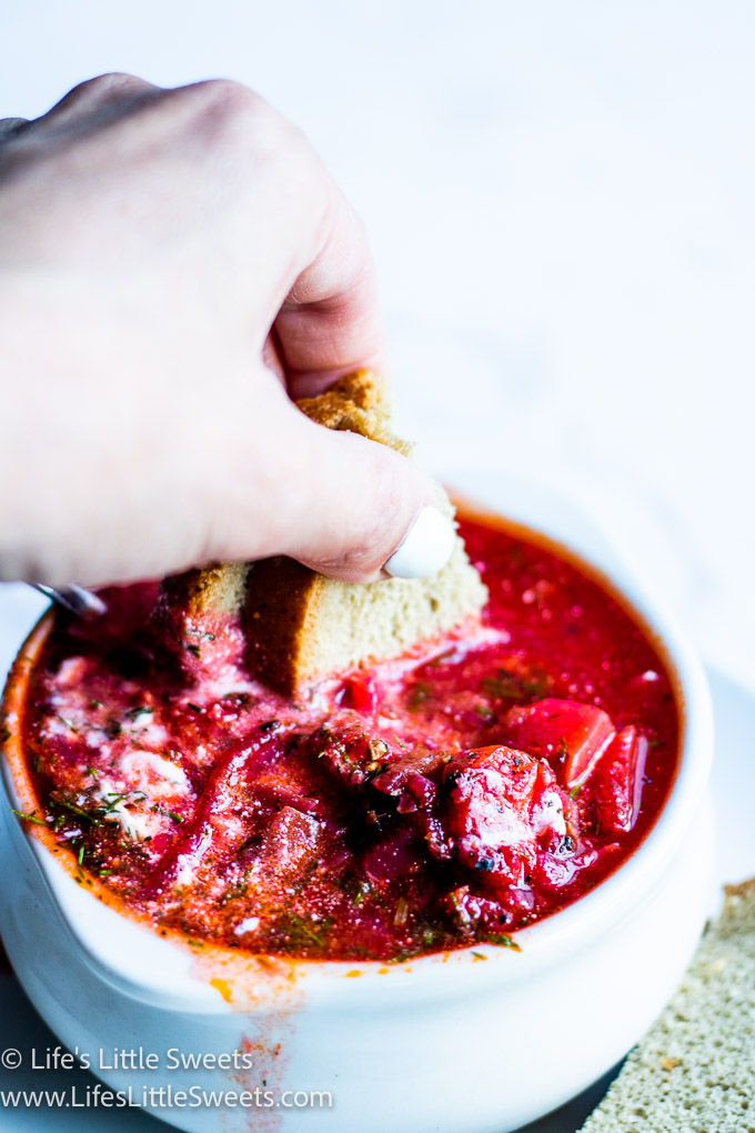 rye bread dipping into a bowl of red Borscht soup with dill and sour cream