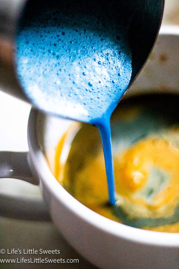 a close up of pouring blue steamed milk into a white mug of espresso